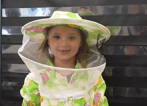 a student in a full beekeeper's outfit smiles