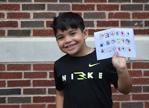 smiling student holds up his "passport" full of colorful stamps